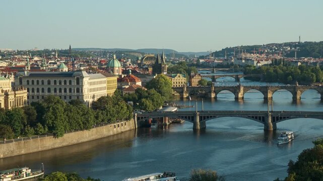 Panoramic view displays famous Prague bridges across the Vltava River. Historic architecture and Charles Bridge highlight the city vista under a sunny sky. Iconic European travel landmark.