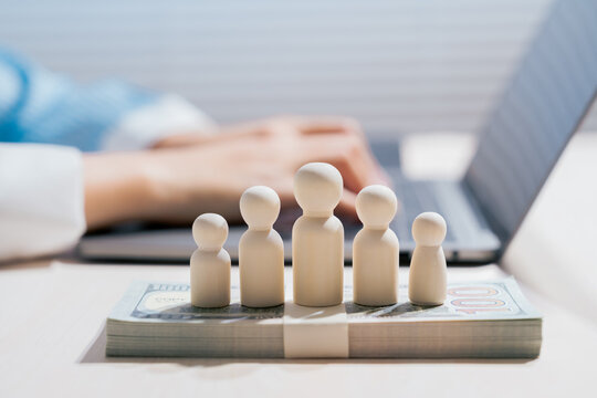 Employee compensation concept. Wooden people standing on money represent payroll and workforce cost; salary, budget, finance, labor, management