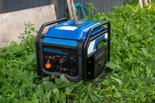Blue portable gasoline power generator standing in green grass outdoors