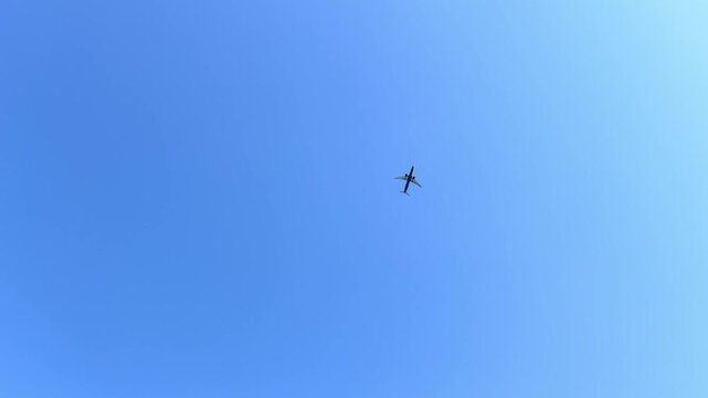 Distant airplane crosses bright blue sky above scattered white clouds