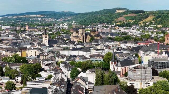 Luftbild von Trier mit der antiken R&ouml;merbr&uuml;cke &uuml;ber die Mosel, umgeben von Stadtarchitektur und gr&uuml;nen H&uuml;geln unter bew&ouml;lktem Himmel an einem Sommertag.