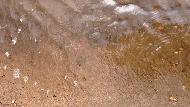 Small river waves wash gently over sand along the shallow shoreline