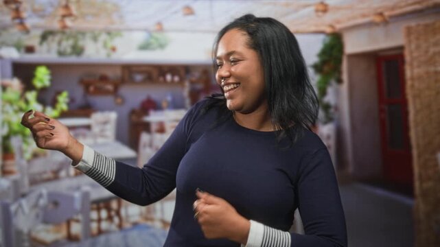 Young woman smiling and dancing, hand holding a small object while swaying in an indoor building cafe scene; joy celebration.