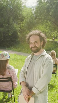 Portrait of middle aged Caucasian man smiling at camera during outdoor art class. Footage is ideal for promoting creative workshops and community education, vertical