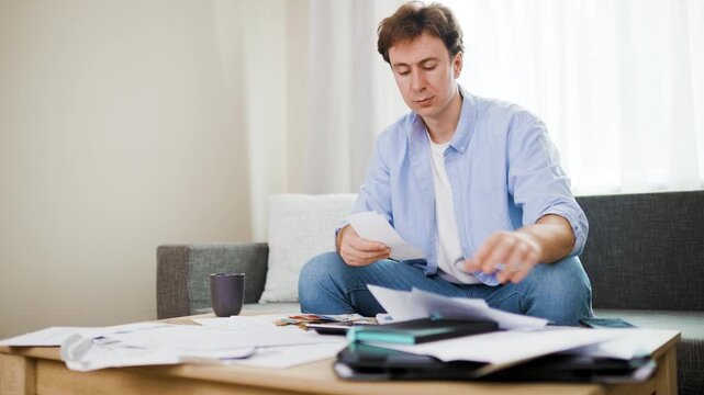 worried man facing a financial crisis due to inflation counts money and checks utility bills and household expenses to manage debt and living cost at home. High quality 4k footage