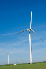 Modern wind turbines in a green field. Majestic white windmills generating clean sustainable energy under a beautiful clear blue sky, capturing the eco-friendly future.  © Roman