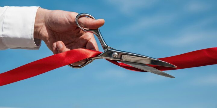 Hand in white shirt sleeve cutting a red ribbon with metal scissors