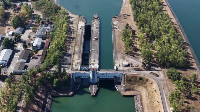 Aerial view of the concrete canal lock structure surrounded by lush green trees and calm water in Hombourg, Grand Est, France.