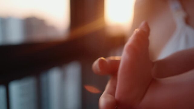 Tender moment captured as a mother lovingly holds her newborn's tiny feet in her hands, with the warm, golden light of sunset creating a beautiful and affectionate atmosphere