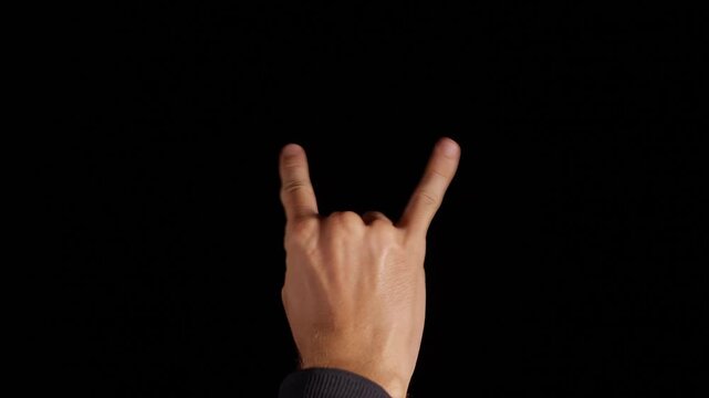 Raised Hand Forms a Horns Gesture Against a Black Background, Expressing Rock Music and Nonverbal Communication