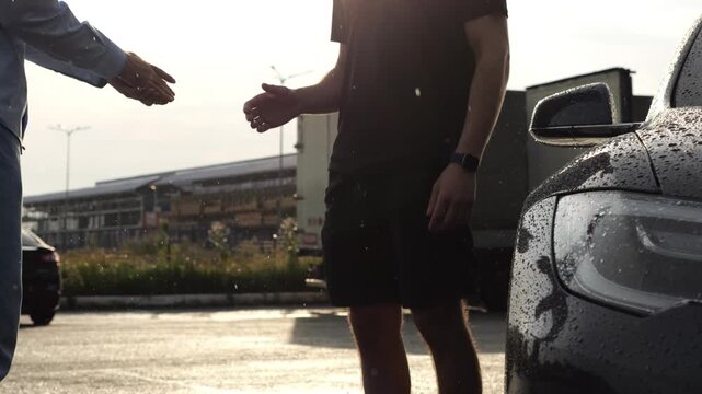 Male arm giving key of car to buyer of modern auto at sunny rainy day. Handshake between salesman and new owner of electric automobile after successful deal. Concept of buy or rent car. Slow motion