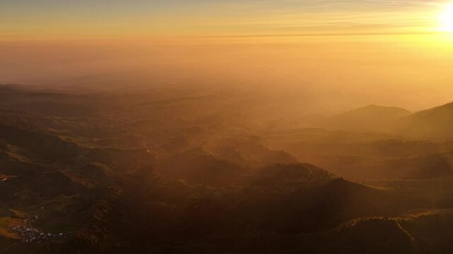 Aerial view of Dieng Plateau at sunrise with rolling hills and golden light filtering through the morning mist in Indonesia.