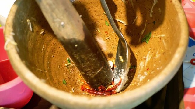 Som Tum spicy Thai food gastronomy close up meal in authentic culinary preparation , combining pounding grinding crushing mashing using a pestle in a clay mortar and metal spoon to release bold