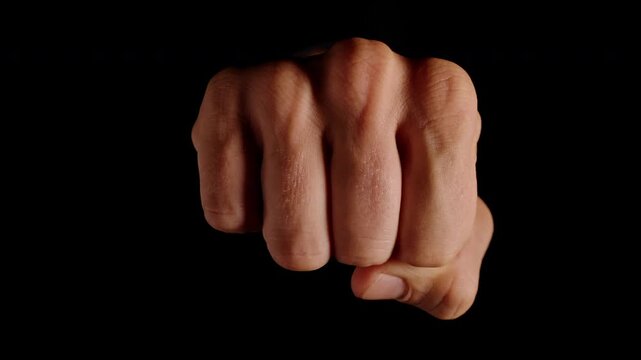 Human Fist Rushes Rapidly Toward the Camera and Slowly Stops in Extreme Close Up against a Black Background, Expressing Aggression, Threat, Violence and Danger
