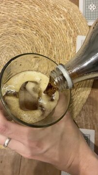 Close up of pouring dark cola into glass with ice and fernet to prepare traditional Argentine cocktail