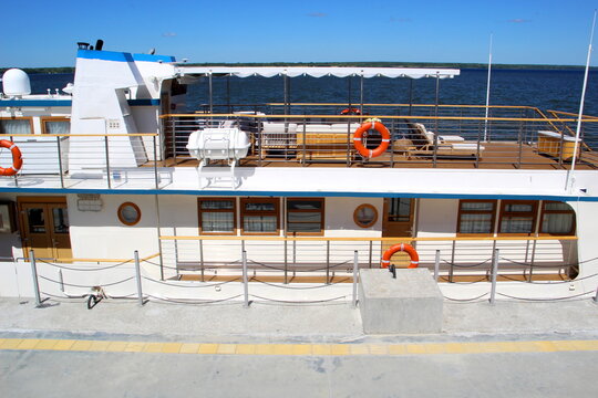 A small motor ship stands at a pier on the river on a sunny summer day.