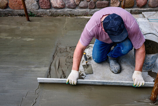 Worker screeding sand bedding to level for laying granite paver blocks. Laying and leveling the floor.