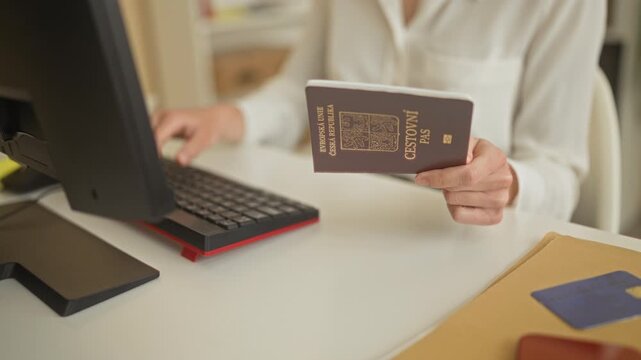 Woman holding passport and typing on keyboard at airport counter with monitor and folder visible; professional focus.