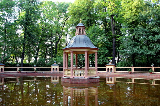 A beautiful retro gazebo surrounded by water stands in the park.