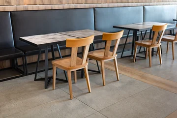 Fotobehang Horeca Interior view of an empty modern cafe featuring wooden chairs and marble patterned tables set against a black leather banquette seating area with warm ambient lighting and contemporary decor design.   © Christos