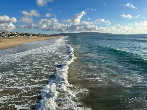 Ocean waves rolling onto a sandy beach under a blue sky with clouds