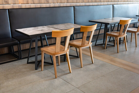 Interior view of an empty modern cafe featuring wooden chairs and marble patterned tables set against a black leather banquette seating area with warm ambient lighting and contemporary decor design.
