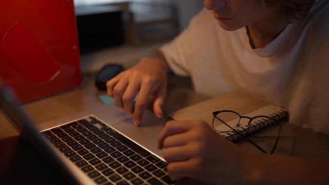 Focused teenager concentrating on schoolwork while using laptop at home with notebook and eyeglasses nearby. Focus, concentration, productivity and academic learning, back to school,education concept