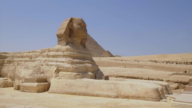 Great Sphinx of Giza with an ancient pyramid in the background under a clear blue sky in Egypt.