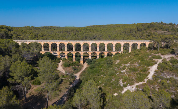 Ancient Roman aqueduct Pont del Diable surrounded by Mediterranean forest near Tarragona, Spain, showcasing double-tiered stone arches against a clear blue sky