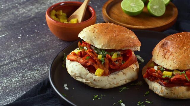 Spicy red pork carne al pastor in a seeded sandwich bun known as cemita