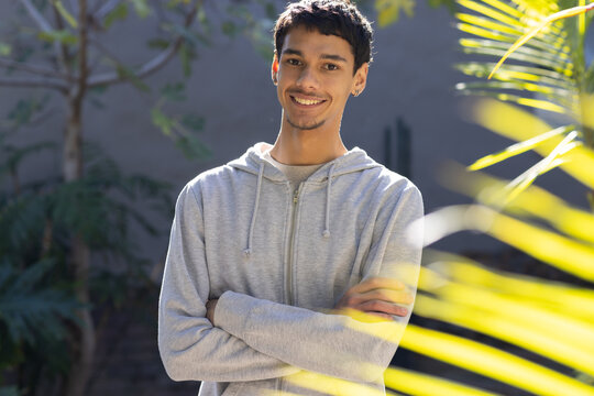 African American man in early 20s standing smiling in garden wearing light gray hoodie, palm fronds