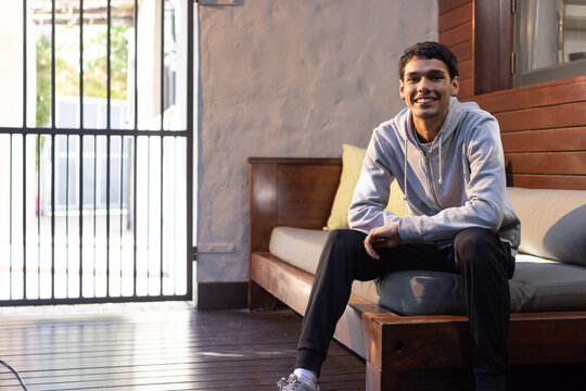African American male sitting on wood bench in sunroom wearing gray hoodie and white sneakers