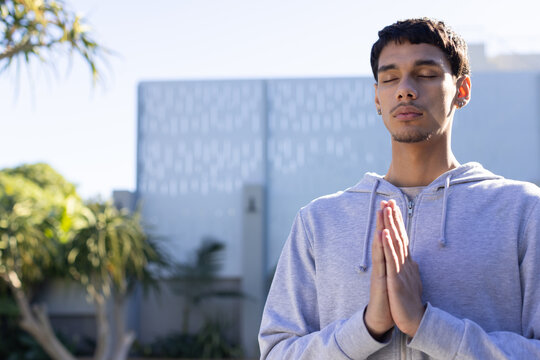 African American man meditating with hands pressed in courtyard wearing gray hoodie, copy space