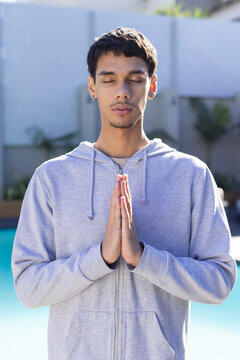 African American man meditating with hands pressed together at poolside wearing light gray hoodie