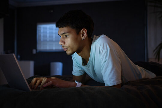 Adult male lying on stomach in bedroom at night using laptop wearing white T-shirt smartwatch