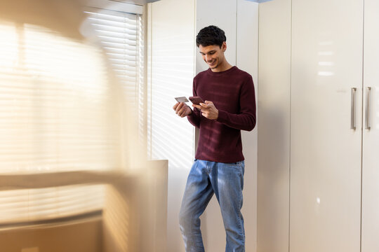 Adult African man standing in dressing area near wardrobe wearing maroon knit holding phone, card