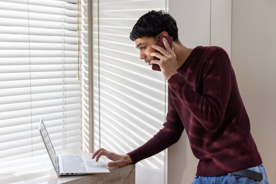 African American man standing at wooden ledge holding phone leaning over silver laptop, copy space