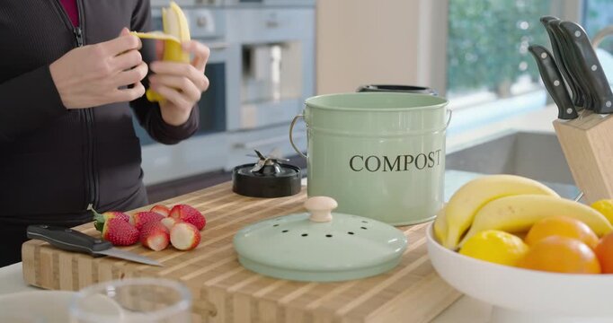 Male in jacket placing compost caddy, peeling, slicing banana on wooden board for snack, copy space