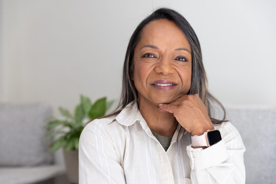 African American mature woman sitting, resting chin on hand in lounge, wearing shirt and smartwatch