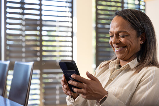 African American mature adult woman sitting at dining table using flip phone smiling, copy space