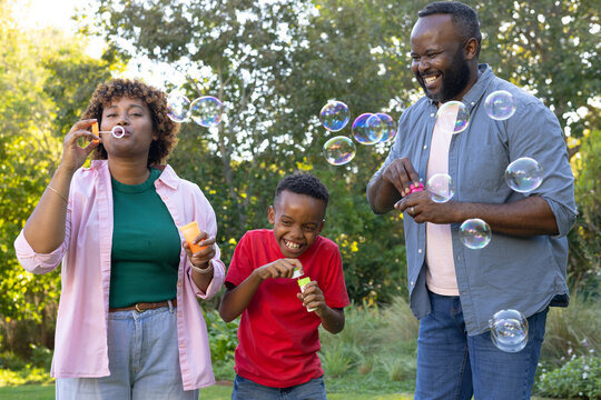 African American family blowing bubbles and laughing in sunny garden with wands, solution bottles