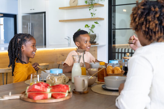 Family of three sitting at wooden dining table in modern kitchen, sharing watermelon breakfast