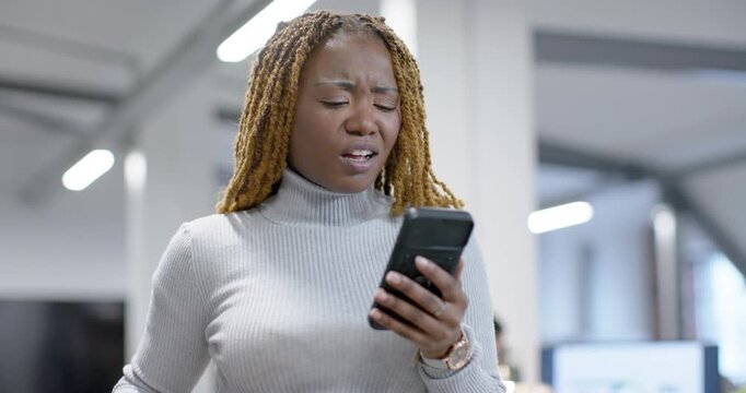Midadult African woman reading new smartphone message in open plan office, reacting, typing reply