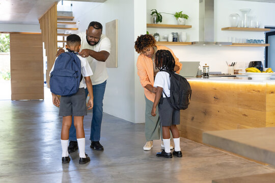 African American family helping children with backpacks at kitchen island with laptop and bananas