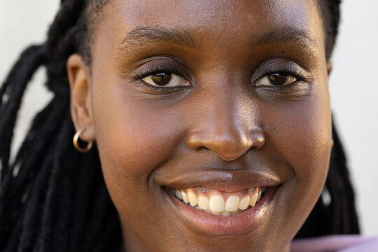 African adult woman smiling, showing teeth in studio close-up with braids, gold hoop, pink top