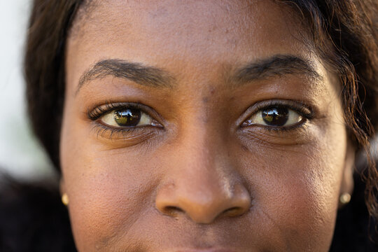 African woman outdoors filling face wearing gold studs, reflecting greenery and figure in pupils