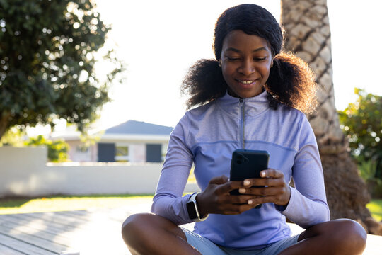 Woman sitting on deck wearing purple top and shorts, holding smartphone and smartwatch
