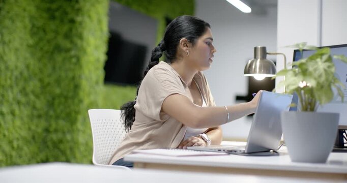 Seeing right file near laptop, Indian woman reaching screen, taking blue pen, taking notes