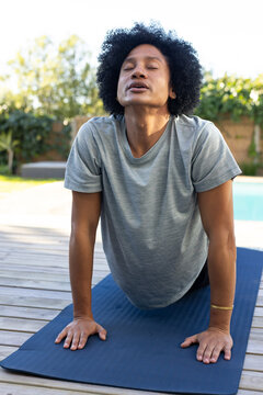 African American man performing yoga backbend on navy mat by backyard pool wearing gray tee, shorts