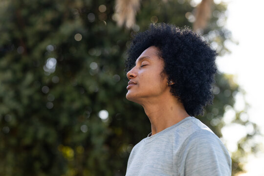 African man standing, closing eyes, tilting head up in park, grey T-shirt, nose stud, copy space